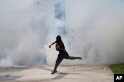 Протестующий бросает камень в струи слезоточивого газа, распыленные полицейскими во время протестов против антимигрантских рейдов, 7 июня 2025 года, Парамаунт, Калифорния, фото AP